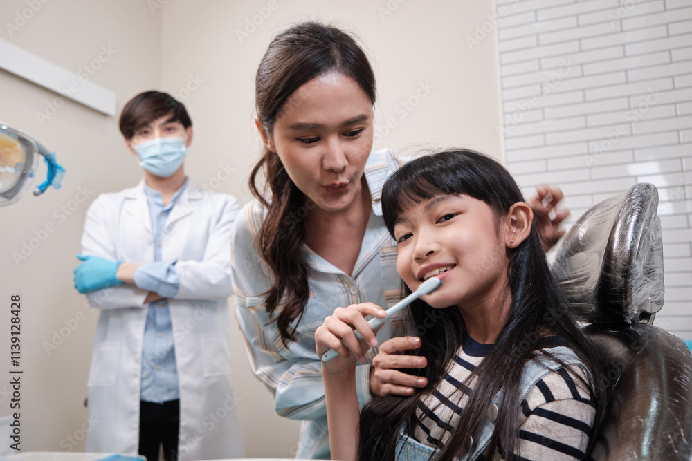 An Asian girl demonstrates teeth brushing to mother and pediatric dentist with toothbrush in dental clinic with happy smile, mouth dentistry hygiene, and orthodontic healthcare work in kid hospital. An Asian girl demonstrates teeth brushing to mother and pediatric dentist with toothbrush in dental clinic with happy smile, mouth dentistry hygiene, and orthodontic healthcare work in kid hospital.
