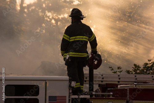 Firefighter standing on fire truck at house fire