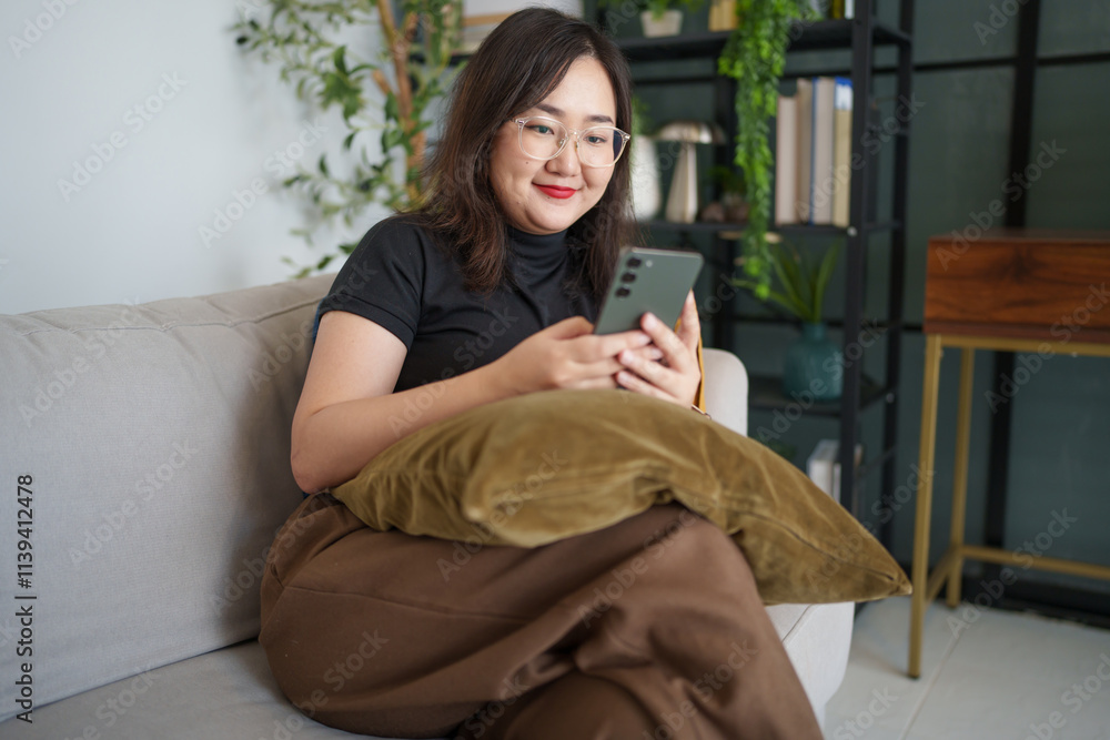 Asian woman sits on sofa using smartphone checking social media, chatting, searching information Asian woman sits on sofa using smartphone checking social media, chatting, searching information