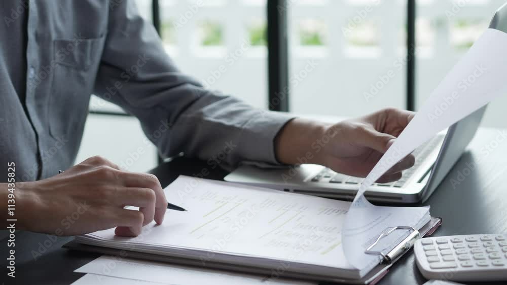 Businessman sits on chair holding pen and checking documents