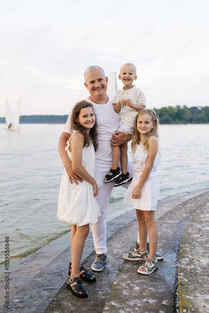 Father and three children are posing for photo on beach. Scene is happy and family-oriented