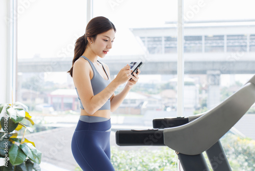 Asian young beautiful woman, sporty active energetic girl in sportswear exercise indoors using smartphone and credit card jogging on treadmill training in living room, health care wellness lifestyle. Free Download Asian young beautiful woman, sporty active energetic girl in sportswear exercise indoors using smartphone and credit card jogging on treadmill training in living room, health care wellness lifestyle. - GFXLoad