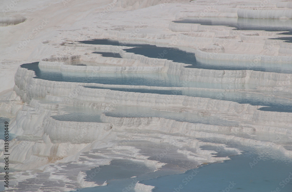 Fototapeta premium Rocky white travertines filled with blue water in Pamukkale, near Denizli, Turkey