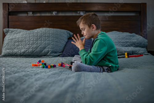 Boy sitting on a bed, focused on colorful toy blocks in front of him photo