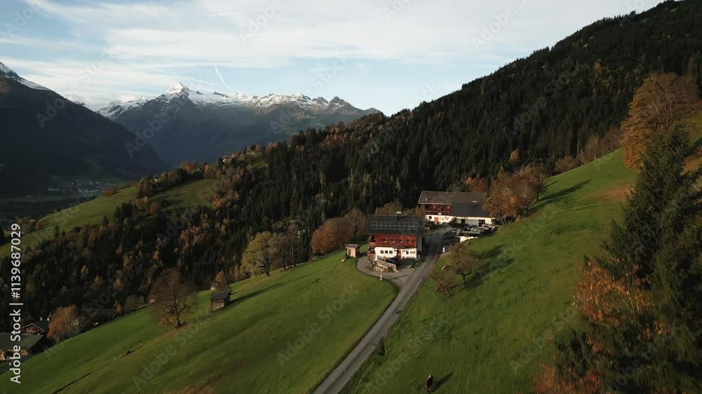 Lush green hills and autumn foliage surround a farmhouse located in the mountains. Snow-capped peaks rise in the background under a clear sky as the sun sets. Lush green hills and autumn foliage surround a farmhouse located in the mountains. Snow-capped peaks rise in the background under a clear sky as the sun sets.
