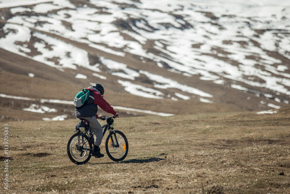 Cyclist riding on a mountain path with snow patches in the backg Cyclist riding on a mountain path with snow patches in the backg
