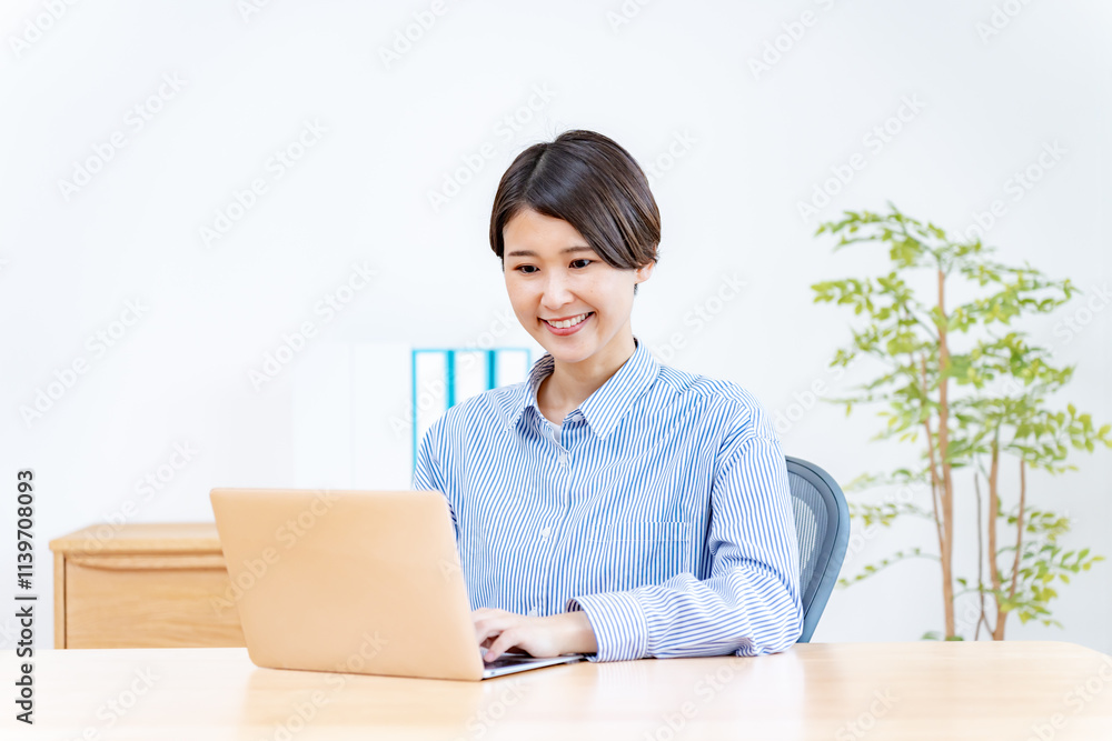 オフィスの椅子に座り笑顔でパソコン仕事をする女性