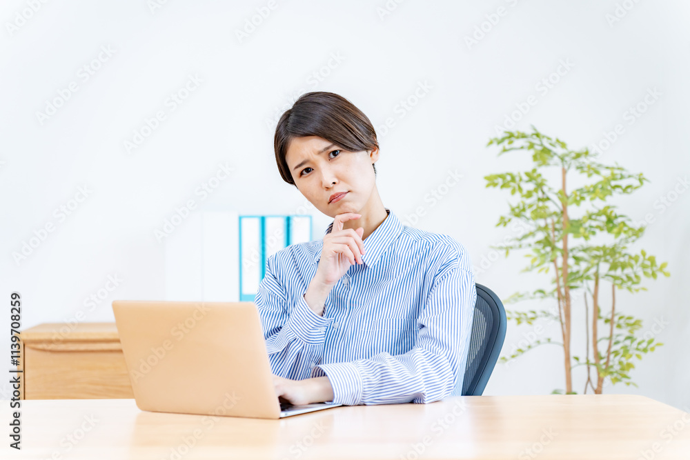 オフィスの椅子に座りパソコン仕事をしながらカメラ目線で考える女性