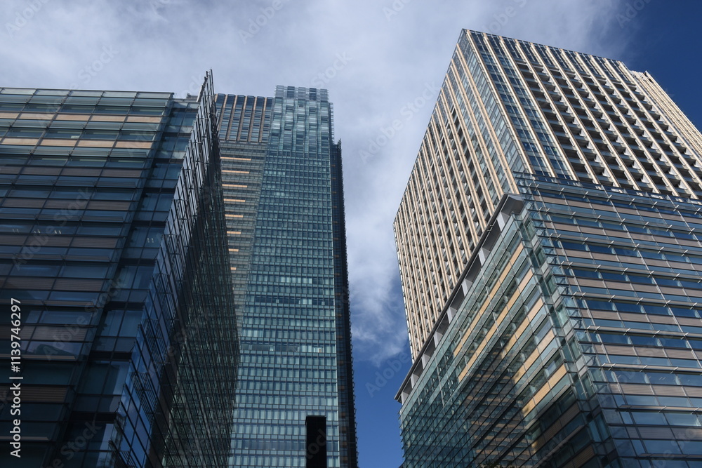 Modern skyscrapers with glass and beige facades rise against a deep blue sky in Roppongi, Tokyo. Modern skyscrapers with glass and beige facades rise against a deep blue sky in Roppongi, Tokyo.