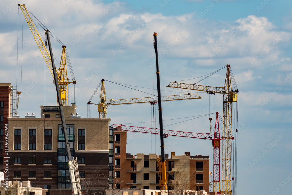 Building under construction with cranes against the background of a cloudy sky. Building under construction with cranes against the background of a cloudy sky.