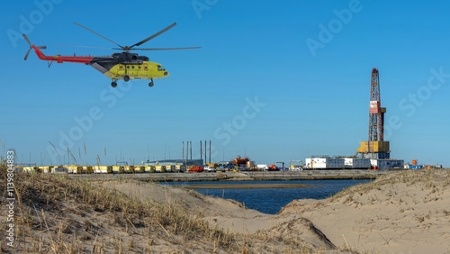 Oil and gas field in the Arctic. Summer. Sandy landscape with small lakes. Drilling rig. Flying helicopter.