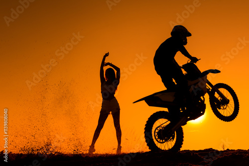 Silhouette of a man on a motorbike on the back wheel, silhouette of a girl in the background. Silhouette of a motorcycle racer with a girl in the background. photo