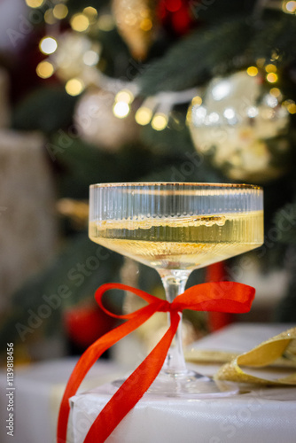 Wide Champagne Glass with a Red Bow on a Blurred Christmas Tree Background
