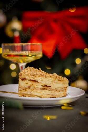 Slice of Napoleon Cake with a Champagne Glass and Christmas Tree Lights in the Background