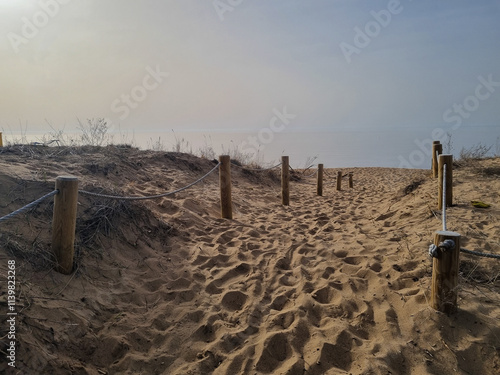 Path through the dune. A sandy path lined with wooden stumps leads to the beach. Sky line joins the water.