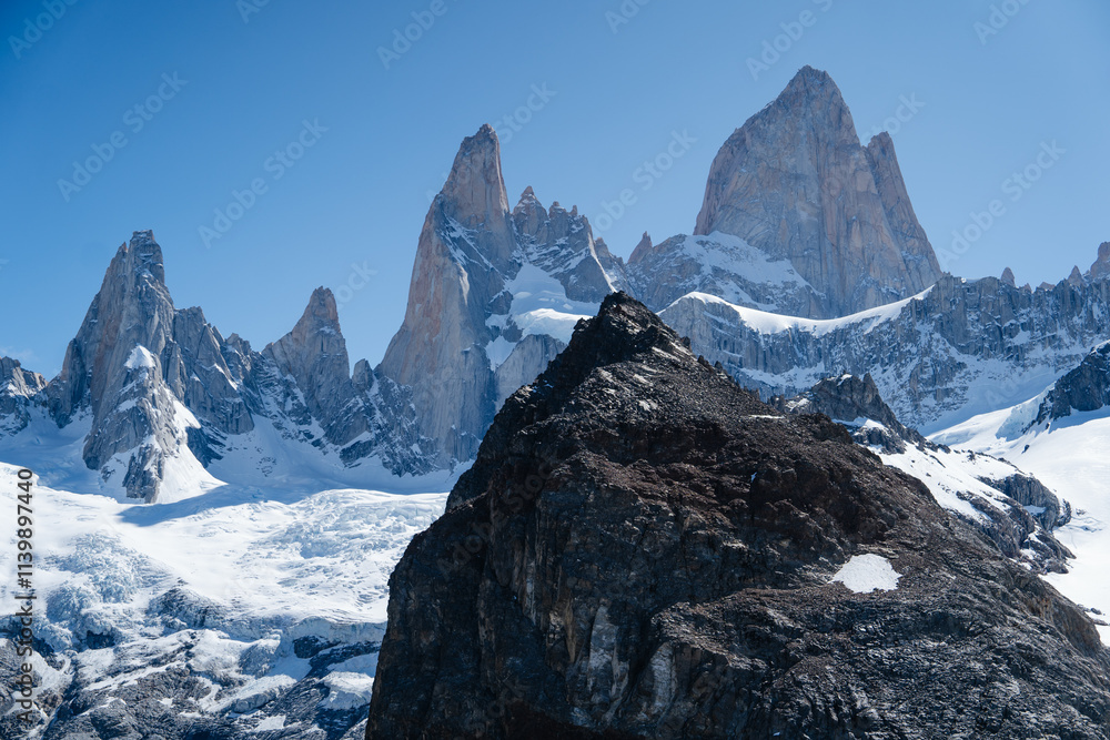 Obraz premium A breathtaking view of the Fitz Roy mountain range in Patagonia, Argentina, captured on a clear day. The sharp granite peaks rise dramatically against the deep blue sky, This iconic landscape