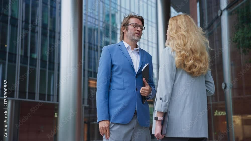 Side view of people talking outside. Caucasian male with business outfit talking to woman. Discussing possible improvements for company. Giving advice or assigning task. End of working day. Side view of people talking outside. Caucasian male with business outfit talking to woman. Discussing possible improvements for company. Giving advice or assigning task. End of working day.