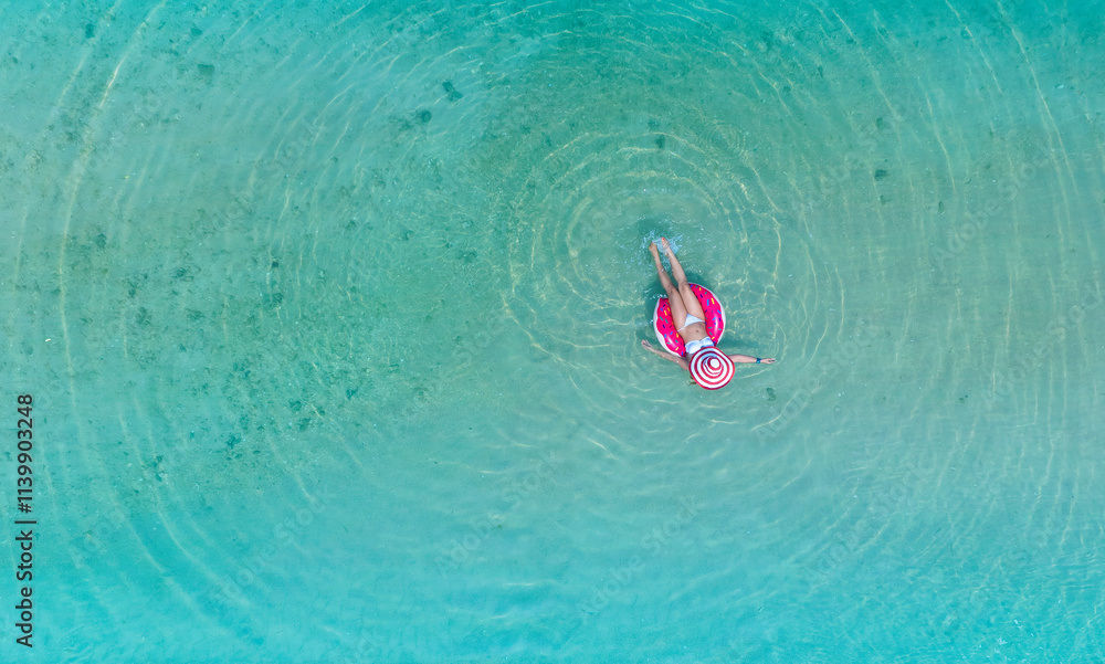 Aerial view with woman in bikini sunbathing as laying on swim ring as blue sea water in background Aerial view with woman in bikini sunbathing as laying on swim ring as blue sea water in background