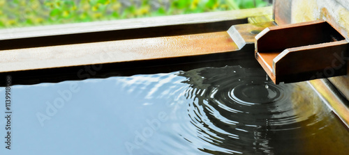 冬の温泉旅行　檜風呂の湯船に湯口から落ちるしずくの美しい波紋
