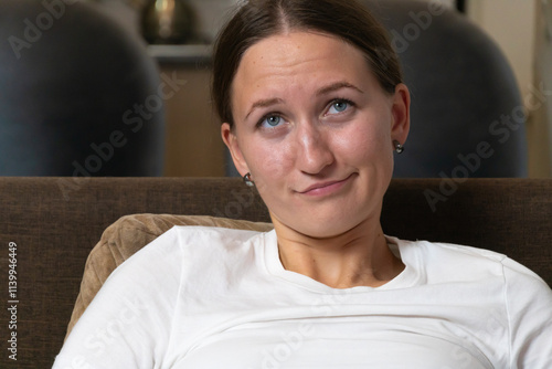 Young woman making a funny face while relaxing on a comfortable sofa in her living room, expressing a playful and carefree attitude