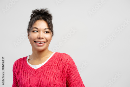 Smiling young woman wearing pink sweater looking away on white background