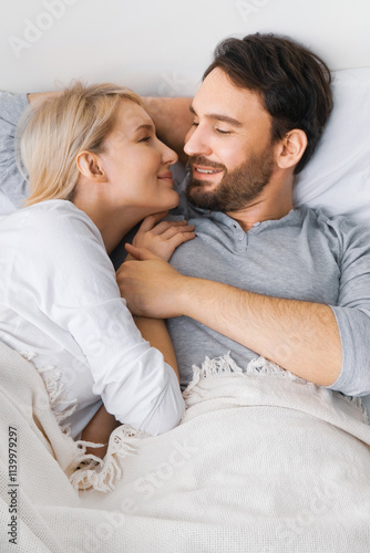 Portrait image - young lovely couple looking at each other, lying on home bed. Cute woman, brunette bearded man in love, relationship, dating, happy family, waiting child concept.