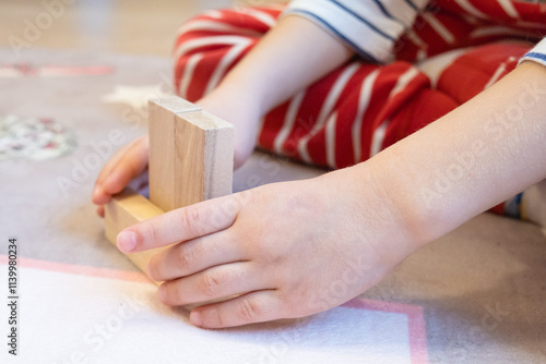 The child plays with wooden bars, making shapes out of them. Eco-friendly toys for children made of natural wood.