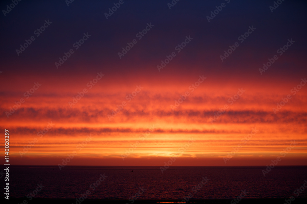 Sunset over a calm ocean, with vibrant orange and red hues in the sky. Dark water reflects the fiery colors. Sunset over a calm ocean, with vibrant orange and red hues in the sky. Dark water reflects the fiery colors.