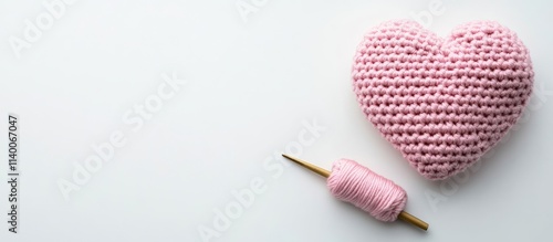 Crocheted pink heart with crochet hook and yarn on white background showcasing handmade craftsmanship and creative hobbies