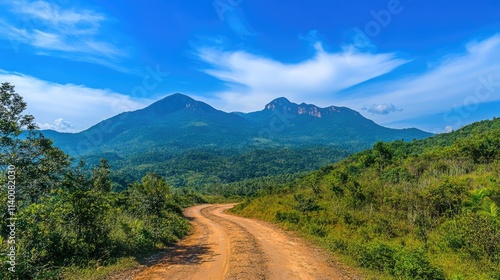 Scenic dirt road winding through lush mountains under a bright blue sky showcasing nature's beauty and tranquility.