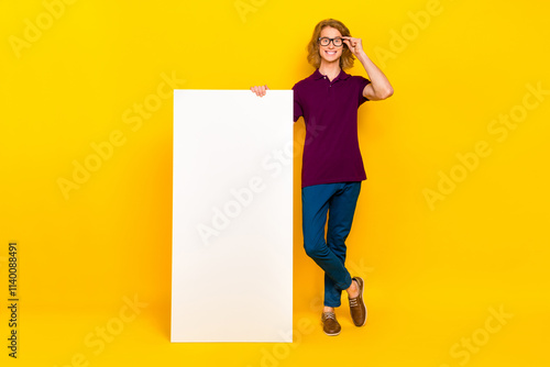 Full body photo of funny ginger guy stand near big telephone wear spectacles t-shirt jeans pants sneakers isolated on yellow background photo