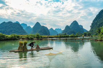 Rural scene of fisherman fishing on wooden raft, surrounded by mountain in sunny day at Phong Nam valley