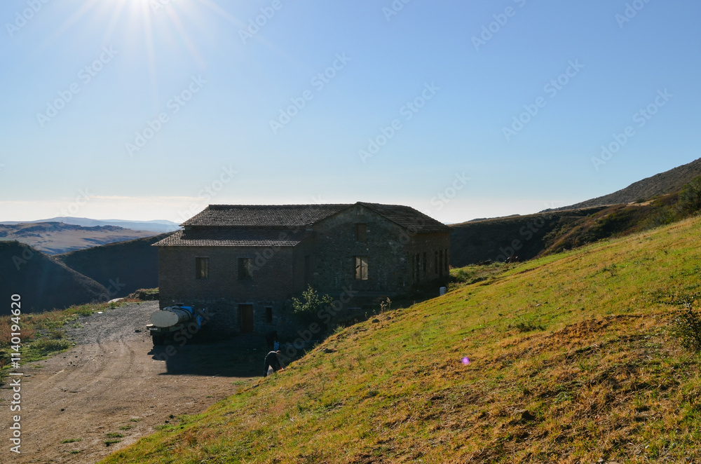 A building situated on a hill, surrounded by grass, with a clear sky and mountainous background reflecting a rural landscape A building situated on a hill, surrounded by grass, with a clear sky and mountainous background reflecting a rural landscape