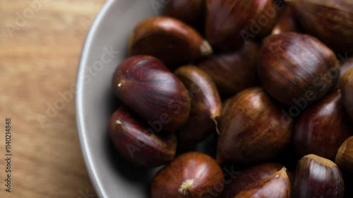 Wallpaper Mural Whole unpeeled raw chestnut fruits with dark brown shells falling into a ceramic bowl on textured wooden table. Slow motion Torontodigital.ca