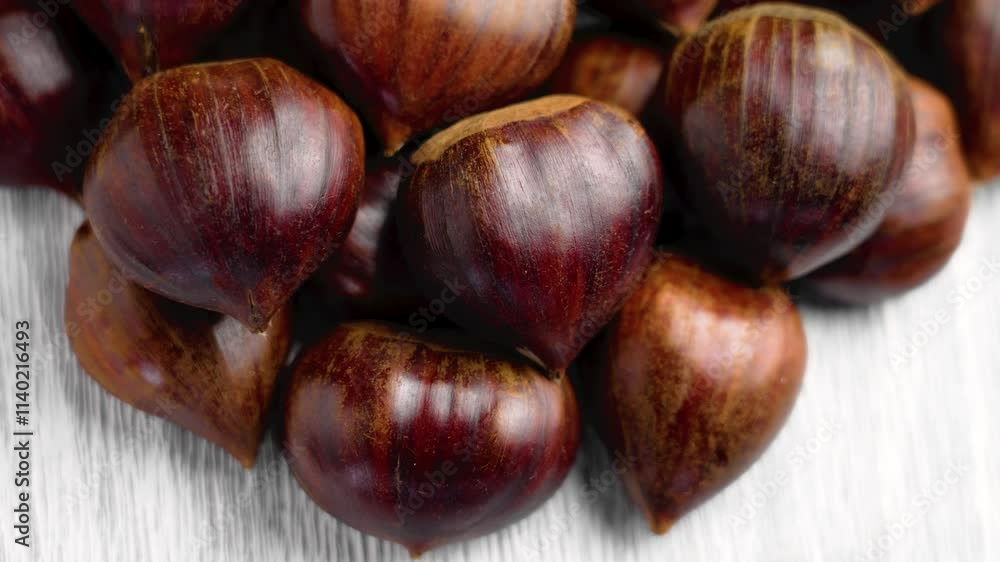 Pile of unshelled organic chestnuts with brown shells. Close-up shot on a cracked textured light wooden background. Top view. Rotation Pile of unshelled organic chestnuts with brown shells. Close-up shot on a cracked textured light wooden background. Top view. Rotation