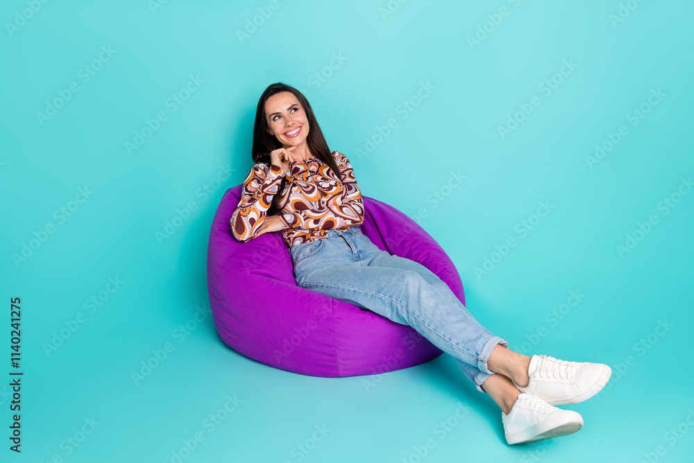 Full length photo of shiny attractive lady dressed retro shirt sitting bean bag look empty space isolated blue color background Full length photo of shiny attractive lady dressed retro shirt sitting bean bag look empty space isolated blue color background