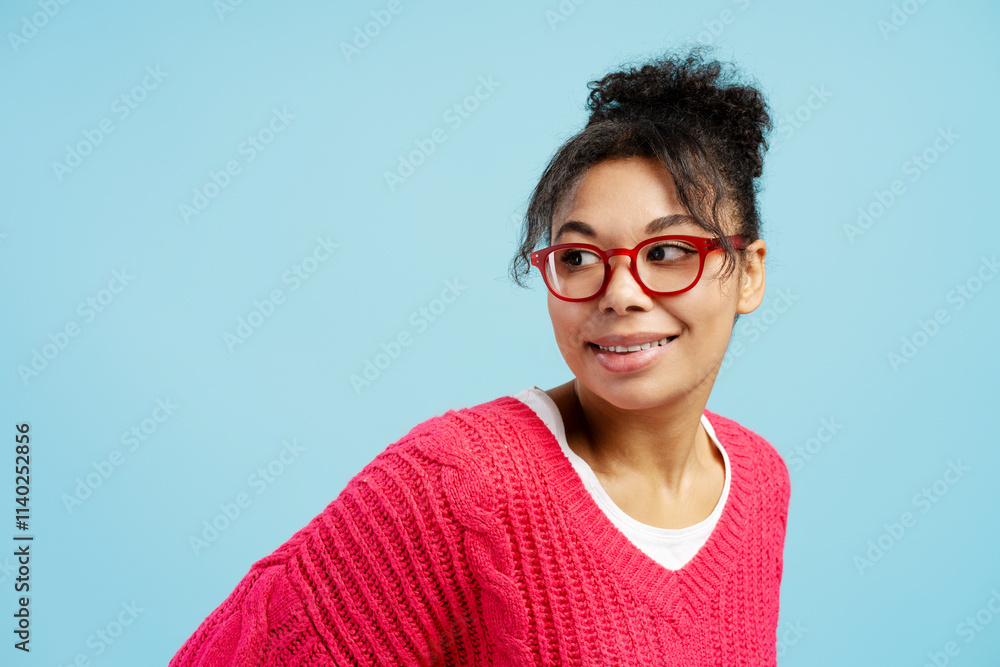 Curious young woman wearing red glasses and pink sweater looking away on blue background Curious young woman wearing red glasses and pink sweater looking away on blue background