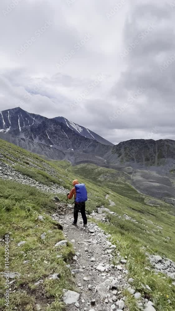 A young man with a backpacker walks a mountain trail during the rain. Trekking in the mountains in summer