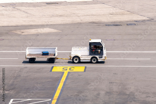 High angle view one baggage tractor-trailer (baggage tow tractor) on a service road on the tarmac of the airport with one suitcase on trolley