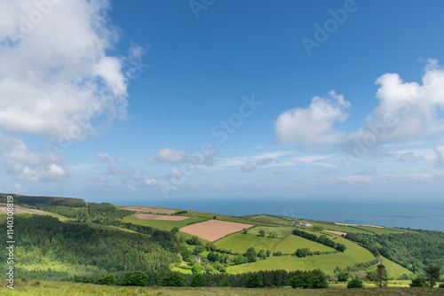 Panoramic high level view over the coastline of Exmoor National Park, west Somerset, UK with rolling agricultural landscape and water of the Bristol Channel against a white clouded blue sky photo