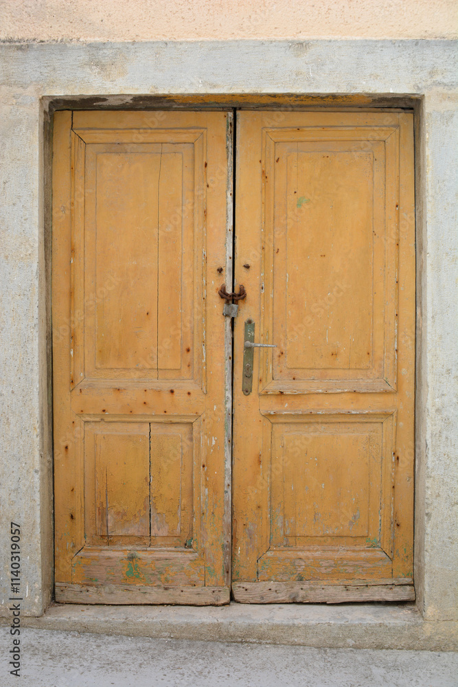 A pair of old, wooden light brown double doors with a metal lock and handle, set in a stone wall A pair of old, wooden light brown double doors with a metal lock and handle, set in a stone wall