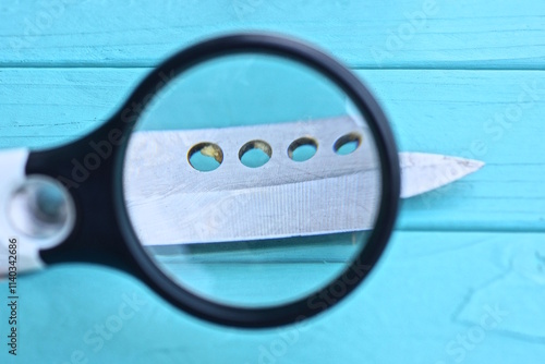 black magnifying glass magnifies one sharp gray iron blade of a folding knife lies on a blue table photo