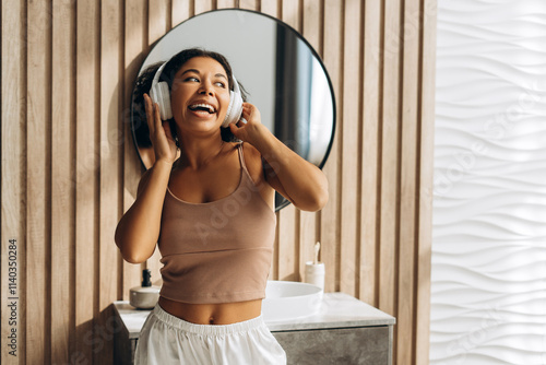 Young woman enjoying music with headphones in modern bathroom photo