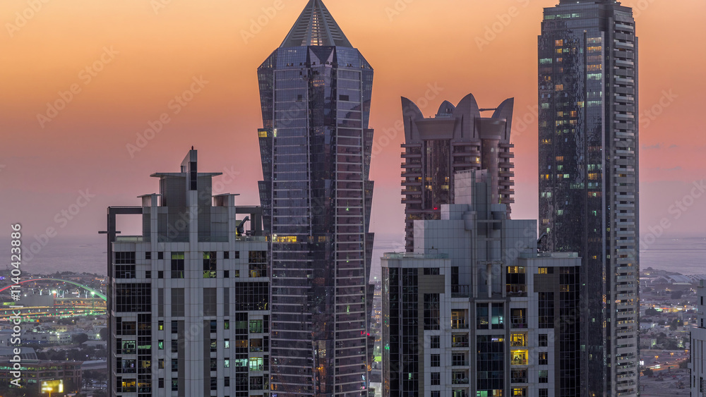Fototapeta premium View of illuminated skyscrapers with lights from windows in Dubai at sunset aerial timelapse