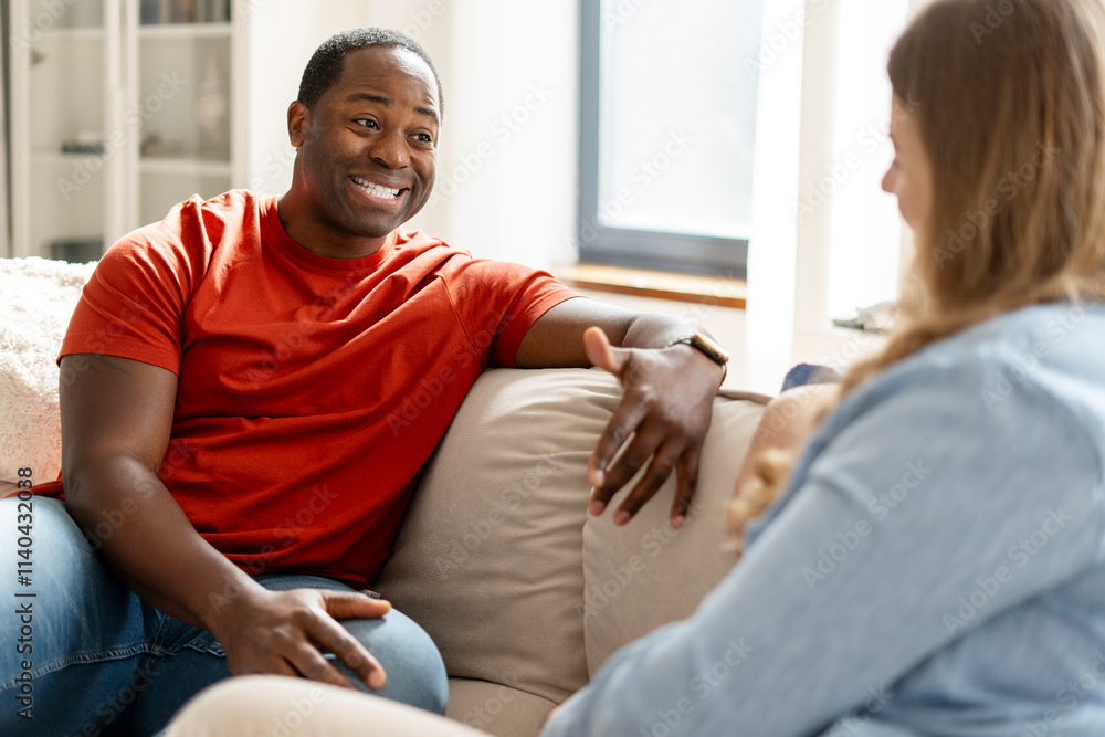 Happy middle aged African American guy looking at woman talking in room at home Happy middle aged African American guy looking at woman talking in room at home