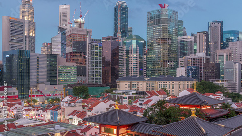 The Buddha Tooth Relic Temple comes alive at night in Singapore Chinatown day to night timelapse, with the city skyline in the background. photo