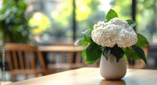 White flowers in a vase on a wooden table surrounded by greenery indoors