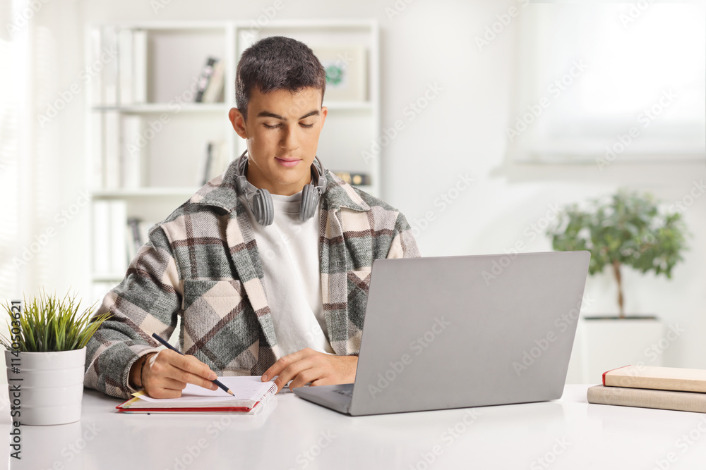 Male student with headphones writing and researching on a laptop computer Male student with headphones writing and researching on a laptop computer