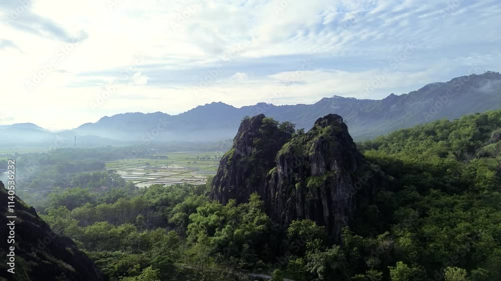 aerial view of ancient limestone rocky mountains, cliffs, and green trees with morning mist surrounded by rice fields. towering rocky hill of Sepikul mountain in Indonesia. aerial view of ancient limestone rocky mountains, cliffs, and green trees with morning mist surrounded by rice fields. towering rocky hill of Sepikul mountain in Indonesia.