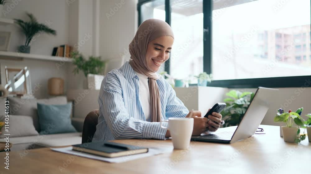 Video of pretty young woman using her mobile phone while working with laptop in the living room at home Video of pretty young woman using her mobile phone while working with laptop in the living room at home